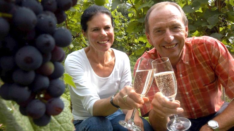 A man and woman pose with glasses of sparkling wine.